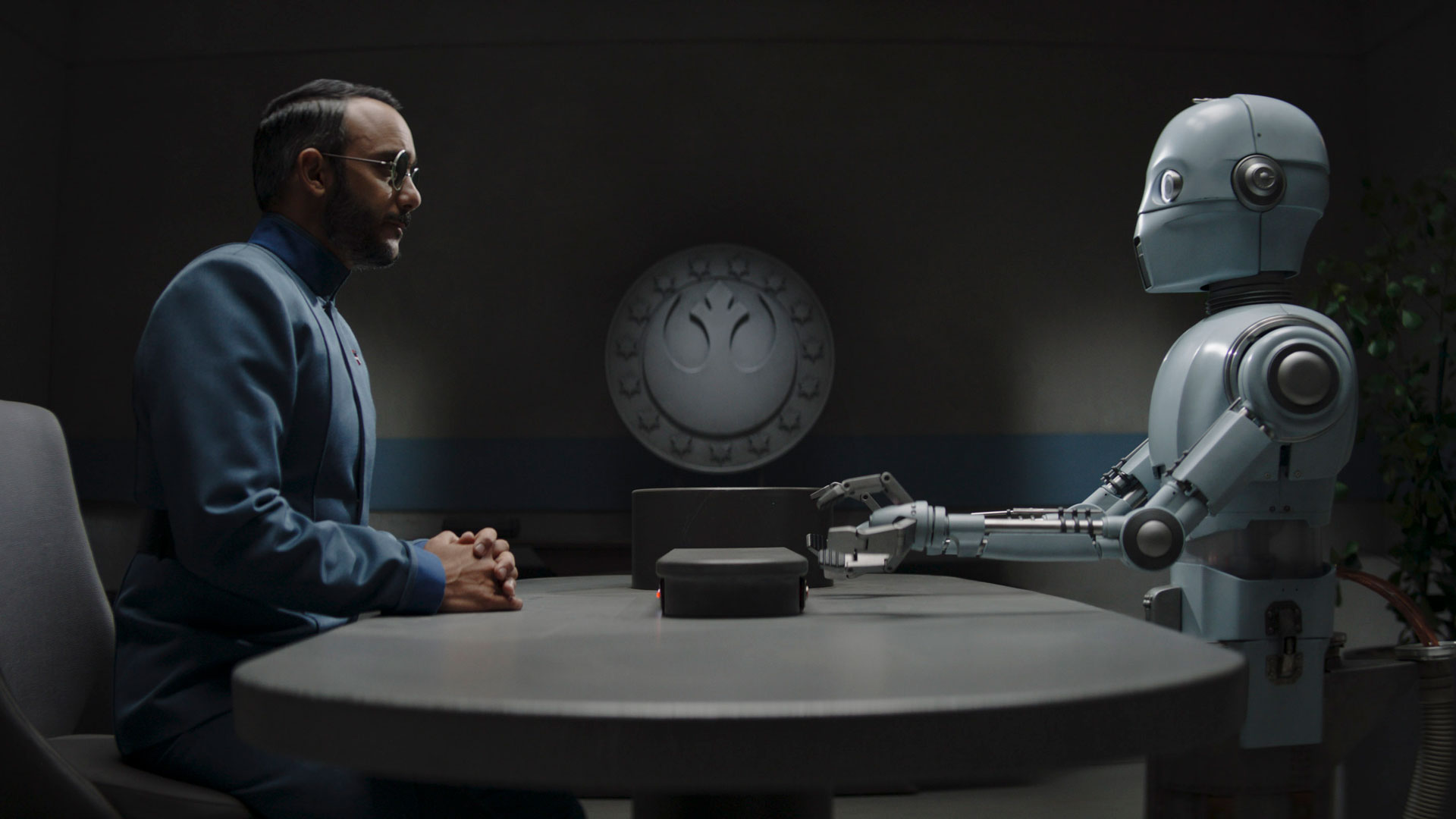 (L-R): Dr. Pershing / Amnesty Scientist L52 (Omid Abtahi) and a parole droid (Regina Hermosillo) in The Mandalorian Chapter 19: The Convert - Lucasfilm Ltd.